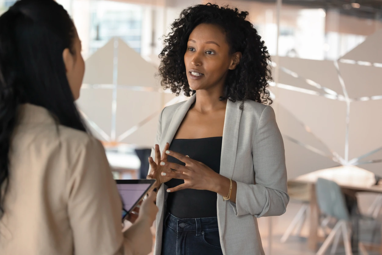 Black woman speaking to another woman in a corporate abroad environment